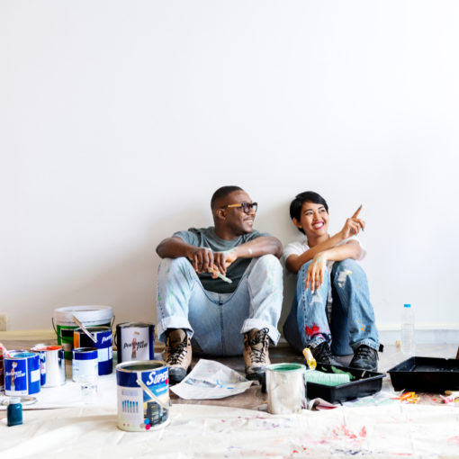 Casal jovem sentado no chão em volta de tintas para pintar o apartamento